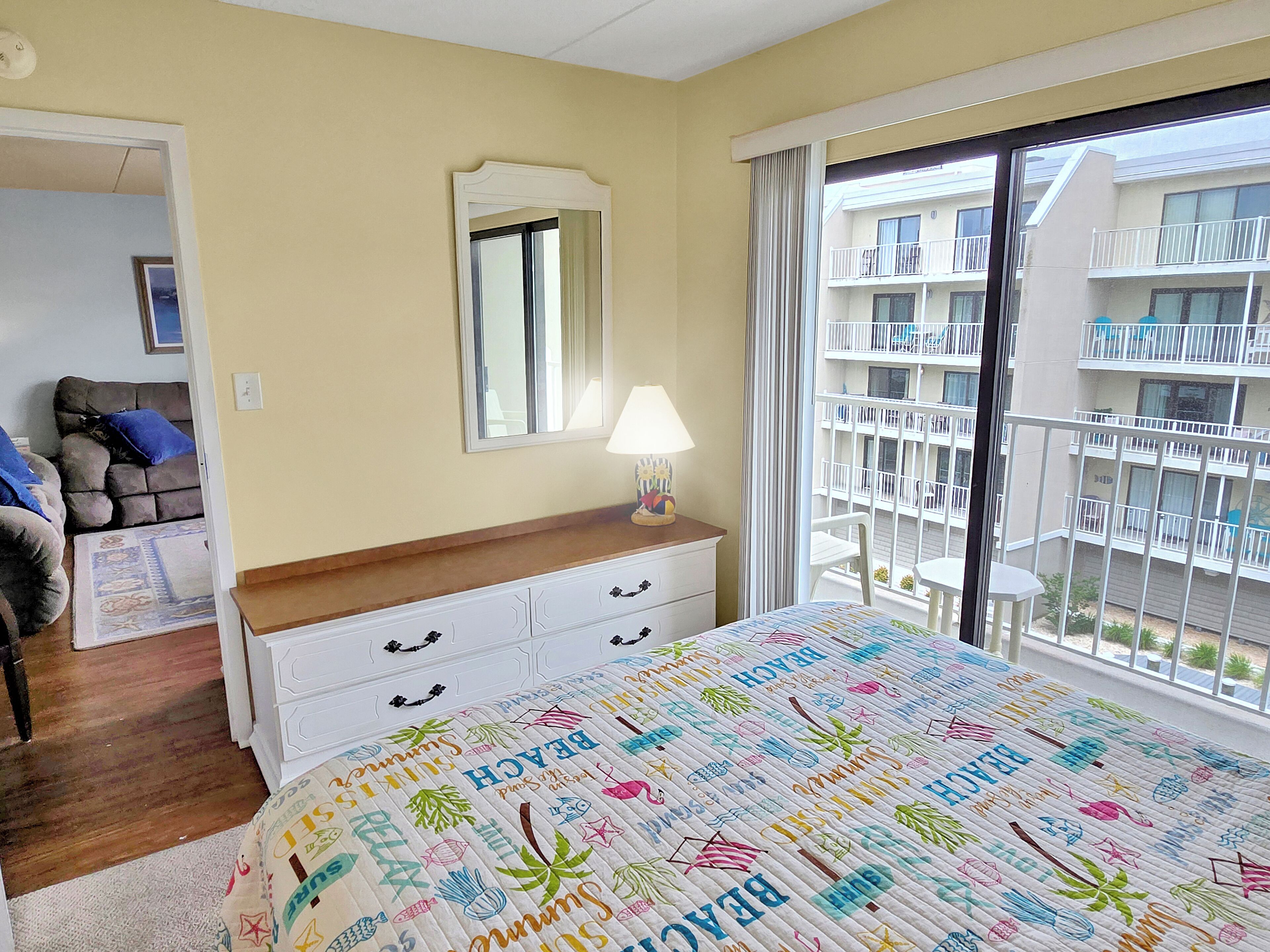 Hotelkamer met een bed, een dressoir, een spiegel, een lamp en een balkon met uitzicht op andere gebouwen.
