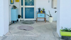 Un edificio blanco con una puerta azul y un letrero de bienvenida. Hay plantas en macetas y un pequeño armario cerca de la entrada.