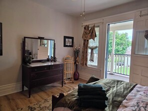 A bedroom with a bed, dresser, mirror, and a view of the outside.