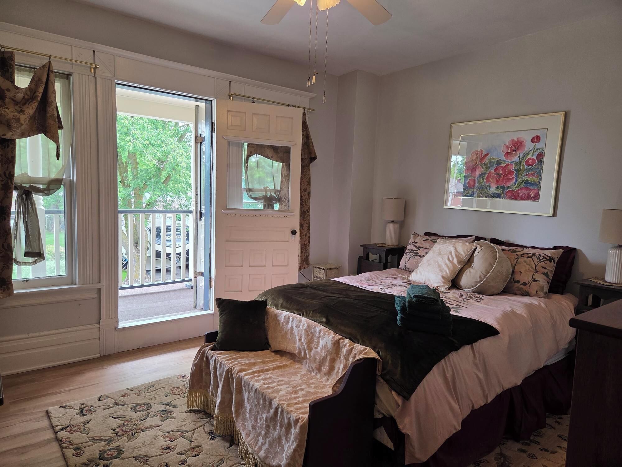 A bedroom with a bed, a chair, a nightstand, a lamp, a painting, and a door leading to a balcony.