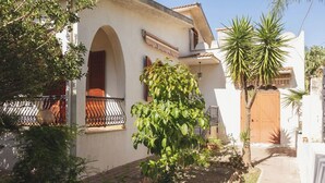 Ein weißes Gebäude mit Balkon, Holztür und einem Garten mit verschiedenen Pflanzen.