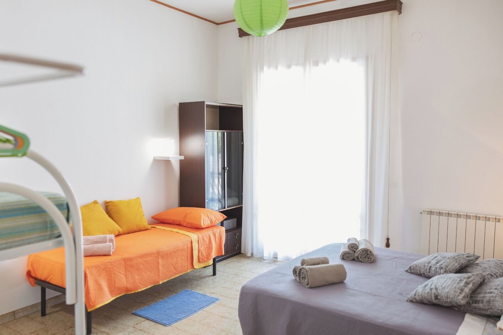 A bedroom with a bed, a wardrobe, a desk, and a window with curtains.