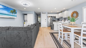 A modern kitchen with white cabinets, a stainless steel refrigerator, and a wooden dining table with white chairs.