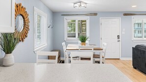A dining area with a white table and chairs, a wooden ceiling light, and a door with a white handle.