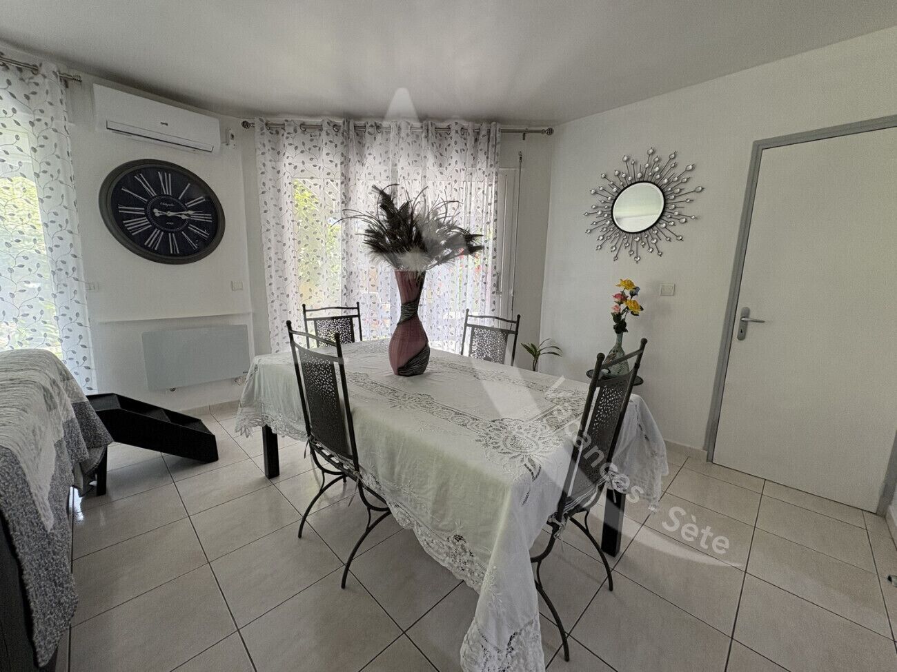 A dining area with a table set for four, a large wall clock, and a decorative mirror.