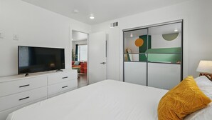 A modern bedroom with a large bed, a TV mounted on a white dresser, and a sliding glass door closet. - Heart of Dallas in Knox Henderson | Sleeps 4 (Dallas)