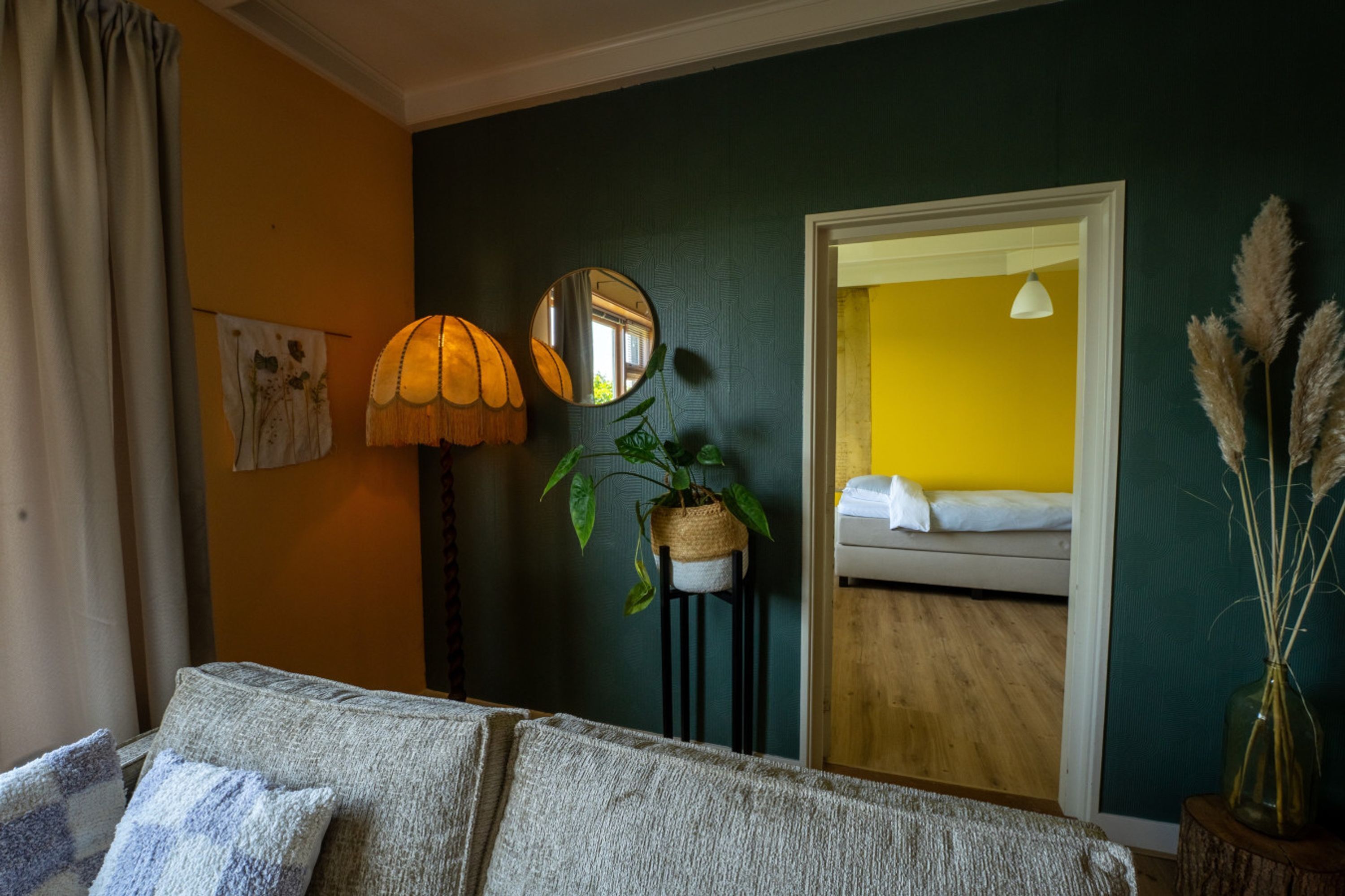 Ein Zimmer mit einem Bett, einer Lampe, einem Spiegel und einer Pflanze.