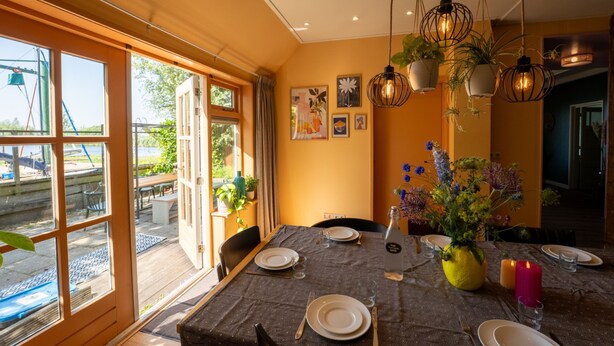 Un coin repas avec une table dressée pour quatre personnes, une grande fenêtre donnant sur l’extérieur et des lampes suspendues.