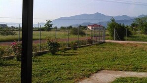 Un espace extérieur clos, comprenant un terrain herbeux, une petite construction et une vue lointaine sur les montagnes.