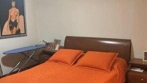 Une chambre à coucher avec un lit en bois, une literie orange, un bureau avec une chaise et un tableau accroché au mur.