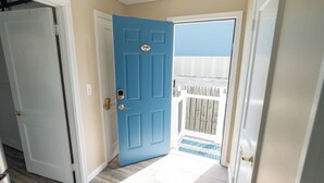 Un pasillo con una puerta azul, una puerta blanca y un timbre blanco.