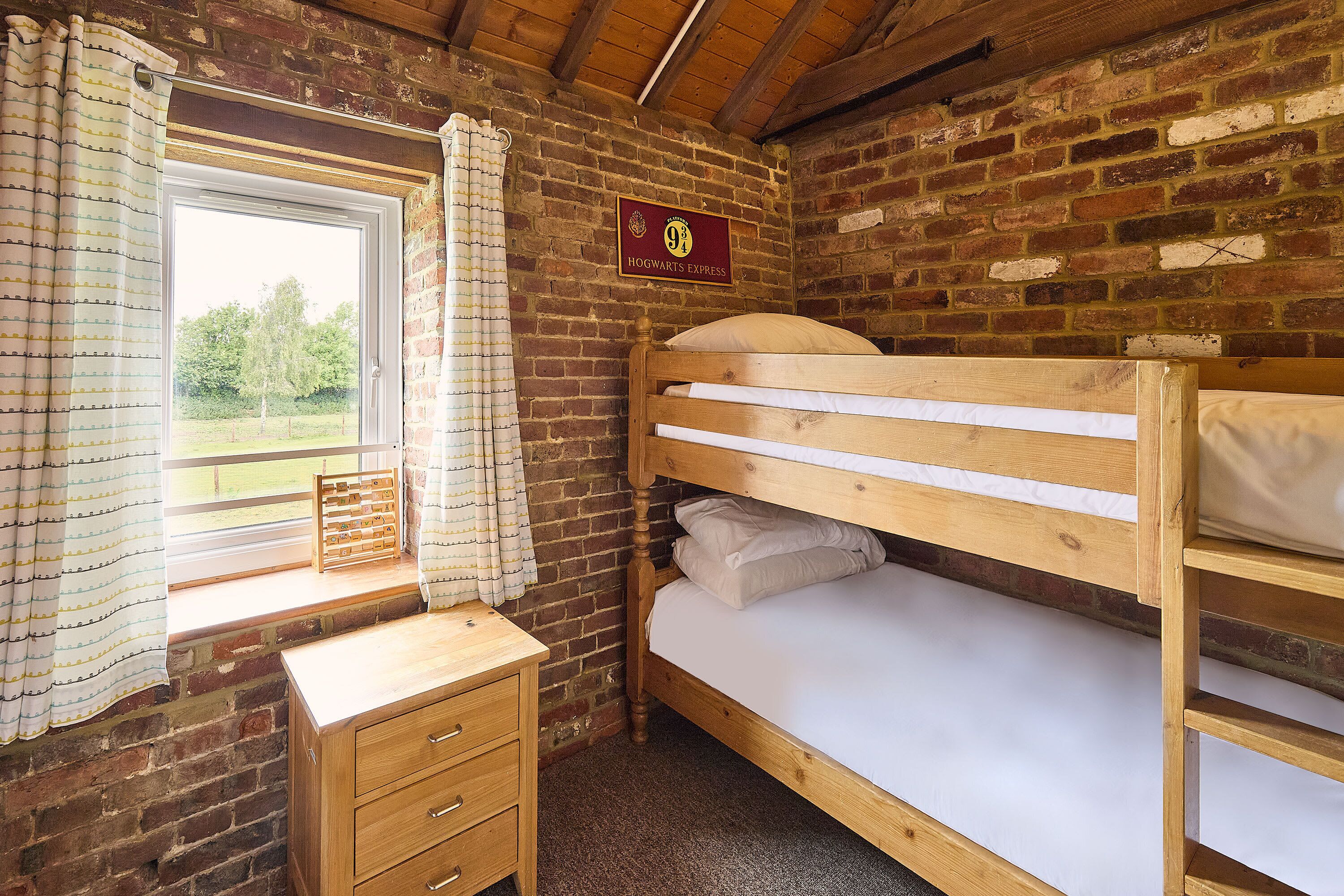 A bunk bed room with a wooden desk, a window with curtains, and a sign on the wall.