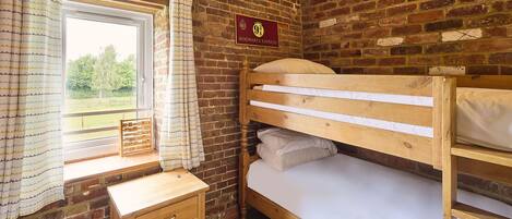 A bunk bed room with a wooden desk, a window with curtains, and a sign on the wall.