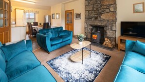 A living room with a blue sofa, a stone fireplace, and a television. - Woodside Family Pet-friendly Holiday Home With Hot Tub (Fraserburgh)