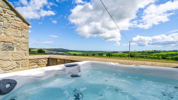 A hot tub with a stone wall and a scenic view of green fields and hills. - Woodside Family Pet-friendly Holiday Home With Hot Tub (Fraserburgh)