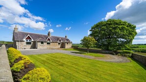 A stone house with a sloped roof and multiple chimneys, surrounded by a well-maintained lawn and a large tree. - Woodside Family Pet-friendly Holiday Home With Hot Tub (Fraserburgh)