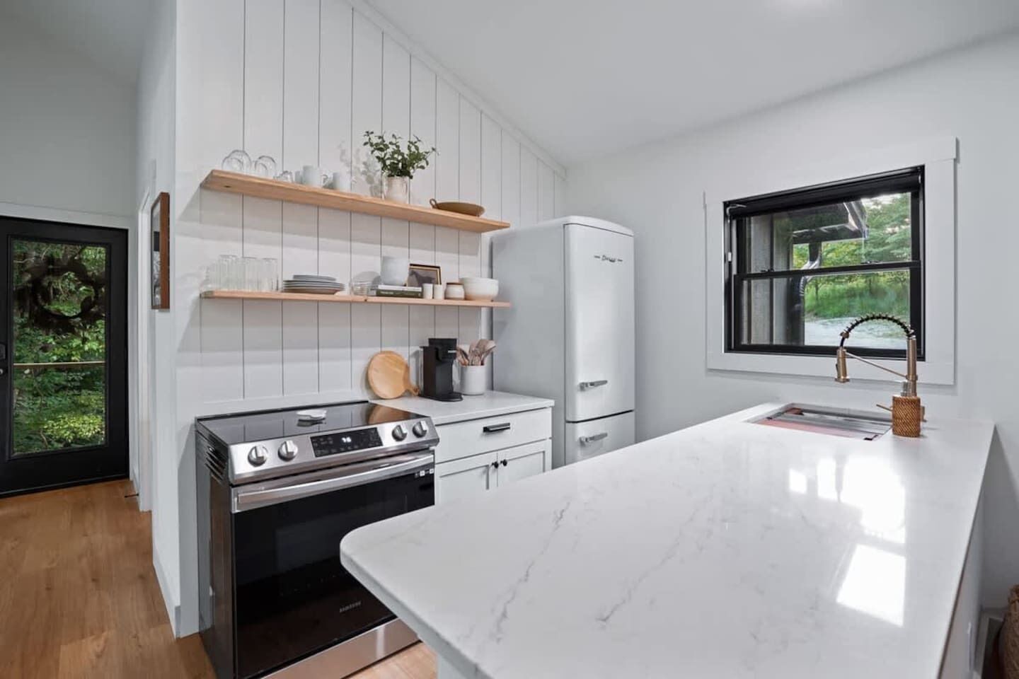A modern kitchen with white cabinetry, a built-in oven, a stove, and a marble countertop.