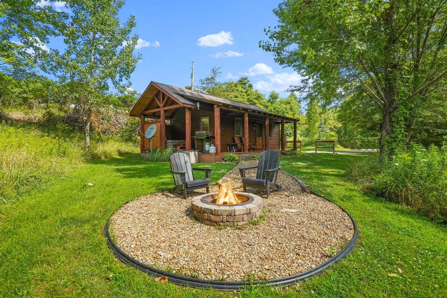 Una cabaña con un hogar y dos sillas Adirondack en el patio delantero.