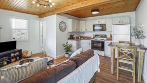 A modern kitchen with white cabinets, a microwave, and an oven. There is a wooden ceiling with exposed beams and a chandelier.
