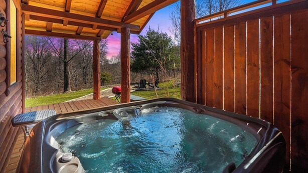 A hot tub under a wooden pergola with a view of a grassy area and trees.