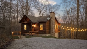A rustic cabin with a chimney, wooden deck, and string lights.