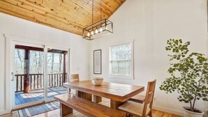 A dining area with a wooden table and benches, a potted plant, and a view of the outdoors through a sliding door.
