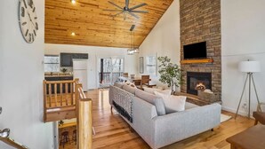 A spacious living room with a fireplace, wooden ceiling, and a dining area with a wooden table and chairs.