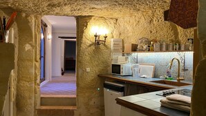 Une cuisine rustique aux murs de pierre, dotée d’un comptoir en bois et offrant une vue sur une chambre à coucher à travers une arche.