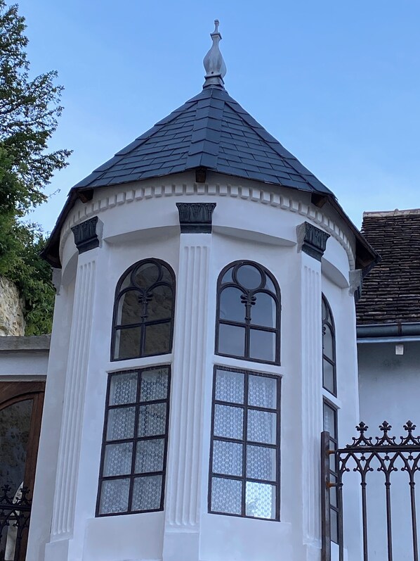 A white building with a dark roof, featuring a central tower with arched windows and decorative elements.