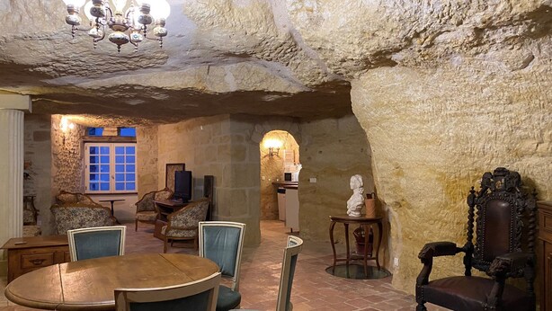 Un espace repas aux murs de pierre, avec une table ronde, des chaises et un lustre.