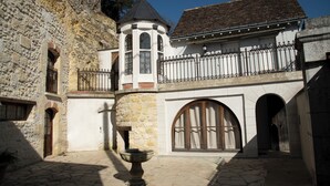 Une cour avec une fontaine en pierre, une tour dotée d’un balcon et un bâtiment entouré d’une grille en fer forgé.