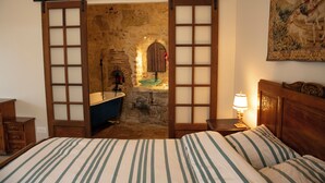 Une chambre à coucher avec un lit, une table de chevet, une lampe et une vue sur une salle de bain à travers une porte en bois.