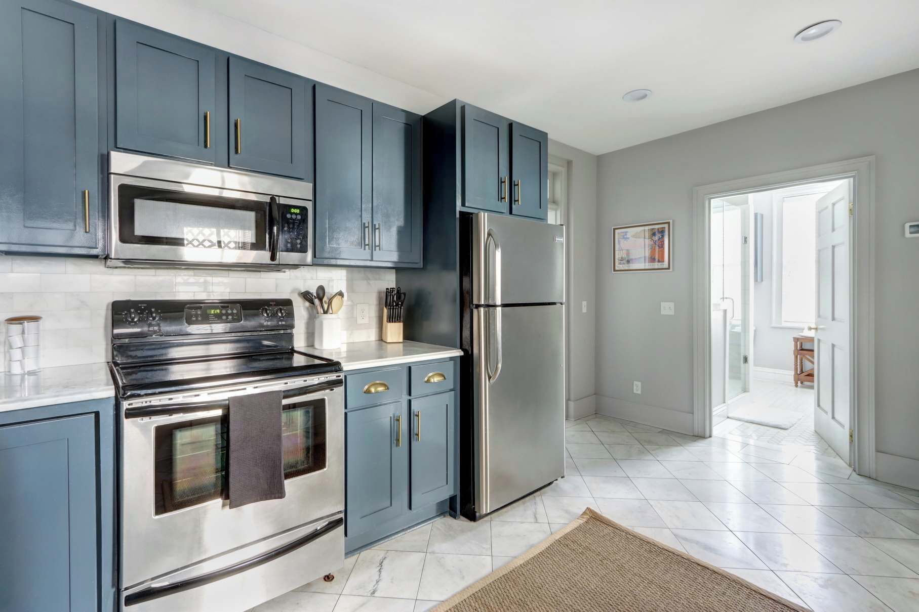 A modern kitchen with stainless steel appliances, blue cabinets, and a tiled floor.