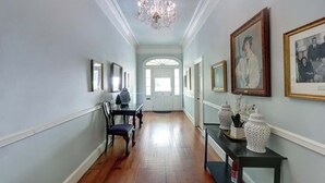 A hallway with a chandelier, framed pictures, and a table with decorative items. - The Murphy House Parlor Suite  | Chippewa View (Savannah)