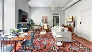 A spacious living room with a dining area, a chandelier, a sofa, and a patterned rug. - The Murphy House Parlor Suite  | Chippewa View (Savannah)