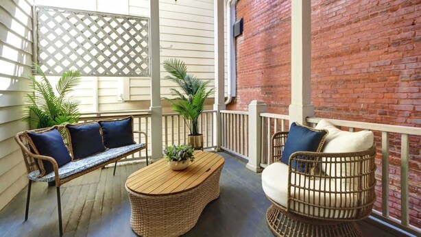 A covered porch with wicker furniture, a wooden table, and potted plants. - The Murphy House Parlor Suite  | Chippewa View (Savannah)