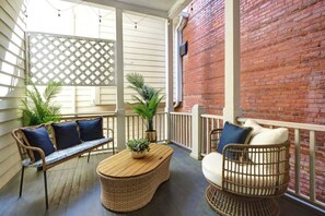 A covered porch with wicker furniture, a wooden table, and potted plants.