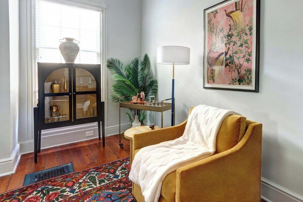 A room with a yellow armchair, a glass cabinet with decorative items, a floor lamp, and a large framed painting.
