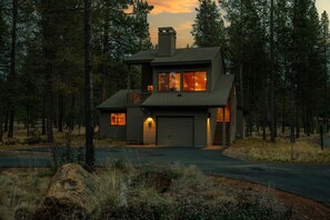 A two-story house with a garage, surrounded by a forest.