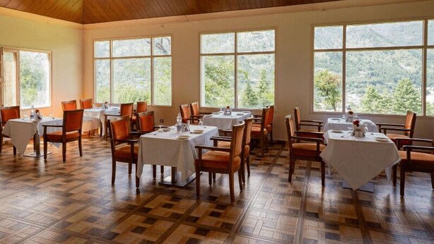 A dining area with tables and chairs, large windows, and a checkered floor. - RishiBhumi Wellness Retreat - Manali (Kullu)