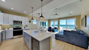 A modern kitchen with white cabinets, a central island, and pendant lighting. - Turtle Paradise | Oceanfront, Beach Access + Private Elevator (Topsail Beach)