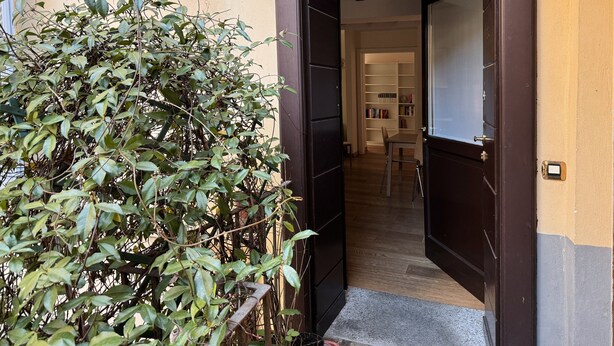 An open door leading to a room with a wooden floor, a chair, and a bookshelf. - 1-bed Flat Near The Duomo (Milan)
