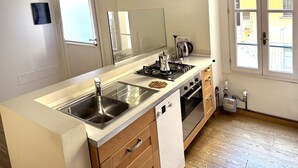 A modern kitchen with a central island, stainless steel appliances, and a view of the outside through a window. - 1-bed Flat Near The Duomo (Milan)