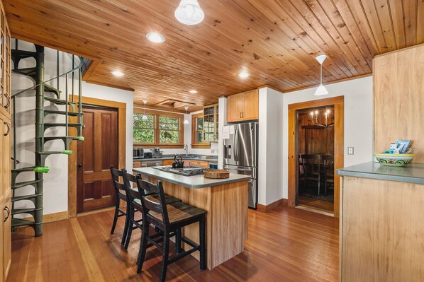 A modern kitchen with wooden cabinetry, a central island with seating, and a stainless steel refrigerator. - Tidebend: River Views and Gracious Comfort (Gloucester)
