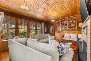 A cozy living room with a wooden ceiling, large windows, and a fireplace. - Tidebend: River Views and Gracious Comfort (Gloucester)
