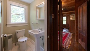 Een badkamer met toilet, wastafel en raam. Een houten deur leidt naar een andere kamer.