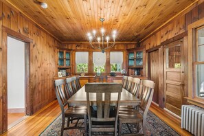 A wooden dining room with a chandelier, large windows, and a view of greenery outside. - Tidebend: River Views and Gracious Comfort (Gloucester)