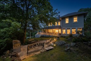 A two-story house with a covered porch, a grill, and a bench in the yard. - Tidebend: River views and gracious comfort (Gloucester)