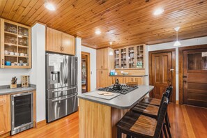 A modern kitchen with wooden cabinets, stainless steel appliances, and a central island with seating. - Tidebend: River Views and Gracious Comfort (Gloucester)