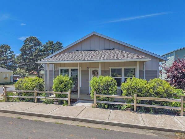 A single-story house with a gabled roof, a front porch, and a small front yard with bushes.